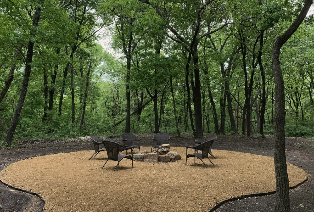 Fire pit circle with wicker chairs under tall trees at Sundowner RV Park